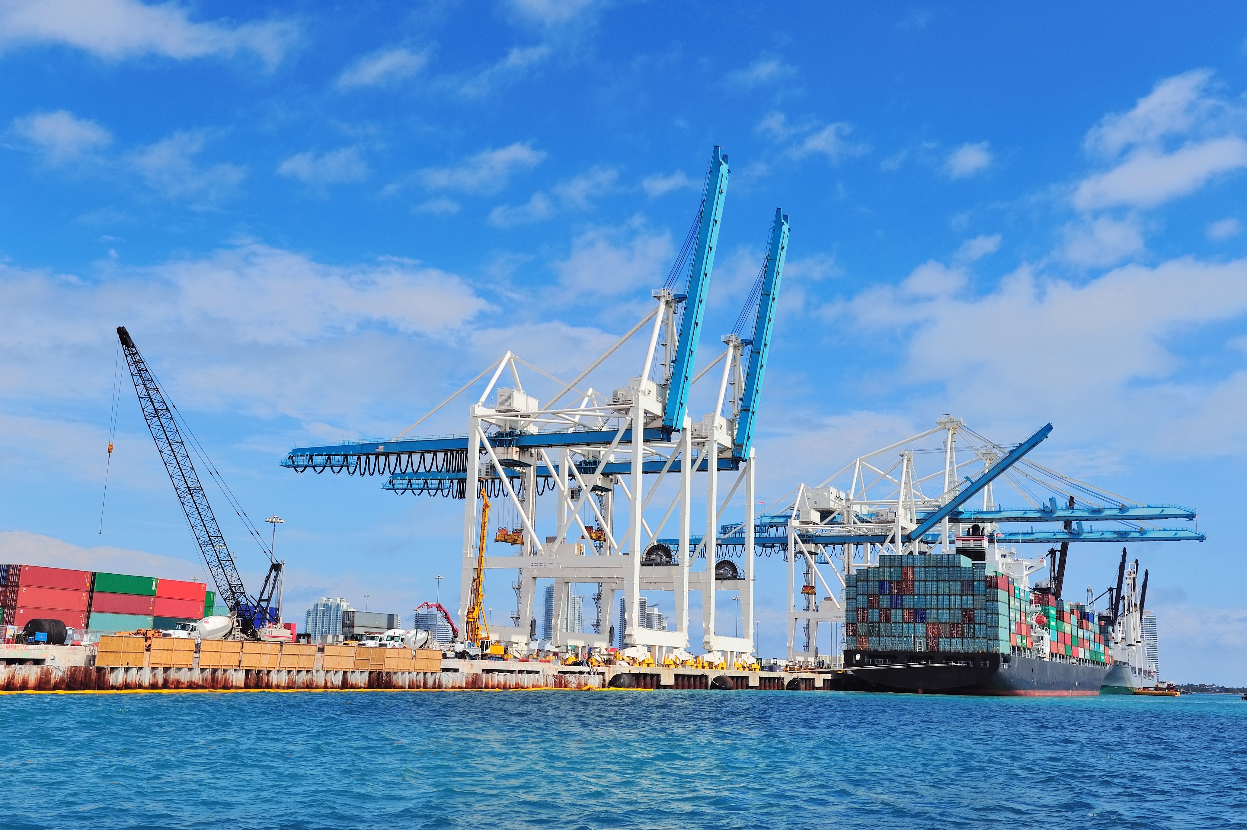 Cargo ship at Miami harbor with crane and blue sky over sea.